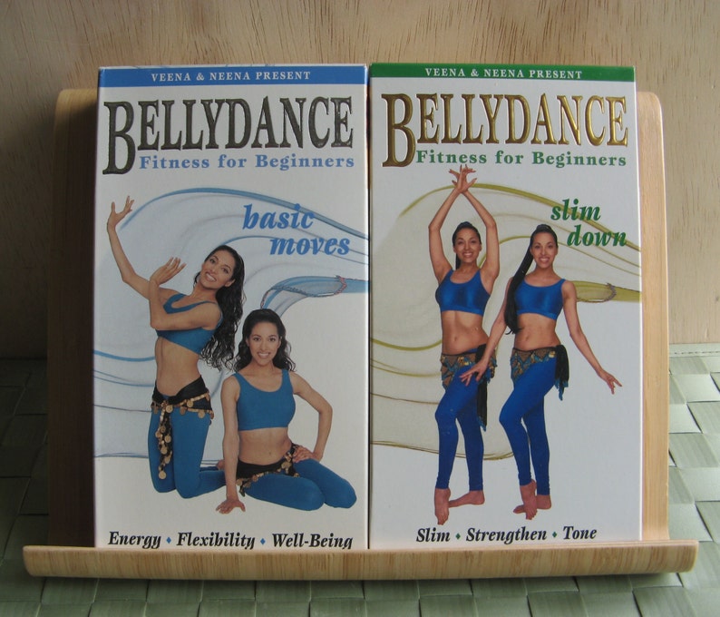 Peut inclure: Deux bo&icirc;tiers de DVD avec des images de femmes en tenue de danse du ventre bleue. Le DVD de gauche est intitul&eacute; "Bellydance Fitness for Beginners: Basic Moves" et le DVD de droite est intitul&eacute; "Bellydance Fitness for Beginners: Slim Down".