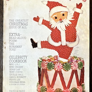 May include: A vintage December 1964 cover of "Good Housekeeping" magazine. It showcases a festive Santa Claus figure crafted from red sweets, positioned above a cake adorned with sweets and liquorice. The cover also features the text "The Greatest Christmas Issue of All."
