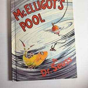 May include: A hardcover book titled "McElligot's Pool" by Dr. Seuss. The cover features a cartoon illustration of a yellow and orange fish, a fishing bobber, and the title in red letters against a blue and gray background.