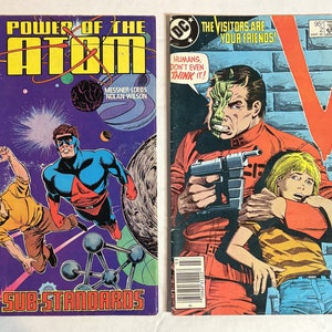 May include: Two comic book covers. The left cover features a blue and red superhero with a yellow lightning bolt on his chest. The cover is titled "Power of the Atom" and has the text "Sub-Standards". The right cover features a red and white "V" with a man in a red jumpsuit holding a woman in a yellow shirt. The cover is titled "The Visitors Are Your Friends!" and has the text "Humans, Don't Even Think It!"