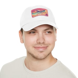 May include: White baseball cap with a colorful patch featuring an airplane flying through a sunset sky. The patch includes the text "Just go". The cap is made of a soft material.
