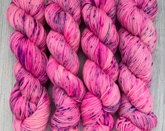 May include: Four skeins of pink yarn with purple speckles. The yarn is arranged in a row, with the skeins overlapping.