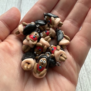 May include: A group of small, handmade polymer clay charms featuring cartoon figures with black hair, brown skin, and large eyes. Each charm has a silver loop for attaching to a necklace, bracelet, or keychain.