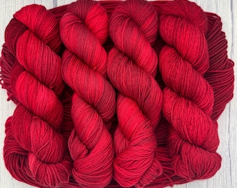 Puede incluir: Tres ovillos de hilo rojo oscuro con un degradado de rojo oscuro a rojo claro.