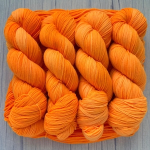 Peut inclure: Gros plan sur plusieurs écheveaux de fil orange vif. Le fil est bien enroulé et semble doux, avec un léger dégradé de couleur. Les écheveaux sont disposés ensemble, suggérant un projet artisanal ou de tricot.