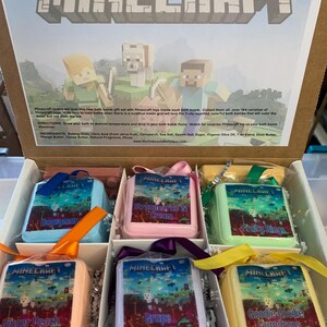 May include: A set of six bath bombs with Minecraft-themed designs. The bath bombs are in a box with a white background and the text "MINECRAFT" in large, bold letters. The bath bombs are in various colors, including blue, pink, green, yellow, and orange. Each bath bomb has a different Minecraft character or design on it. The bath bombs are packaged in a clear plastic bag with a ribbon.