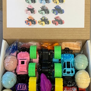 Könnte beinhalten: Eine Box gefüllt mit einem Monstertruck-Geschenkset. Das Set enthält 6 bunte Monstertrucks, 6 Badebomben und ein lila Spielzeug. Die Box hat ein Bild von 12 Monstertrucks auf der Vorderseite mit dem Text "Monster Truck Gift Set".