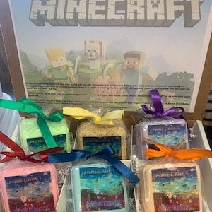 May include: A set of six bath bombs with Minecraft character designs. The bath bombs are wrapped in clear plastic and tied with colorful ribbons. The bath bombs are labeled with different scents, including Black Cherry, Cotton Candy, and Clementine.