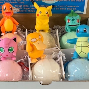 May include: A set of six bath bombs featuring Pokemon characters. The bath bombs are wrapped in clear plastic and are arranged in a white box. The characters include Pikachu, Charmander, Squirtle, Bulbasaur, Jigglypuff, and Psyduck.
