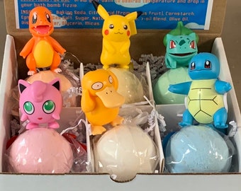 May include: A set of six bath bombs featuring Pokemon characters. The bath bombs are wrapped in clear plastic and are arranged in a white box. The characters include Pikachu, Charmander, Squirtle, Bulbasaur, Jigglypuff, and Psyduck.