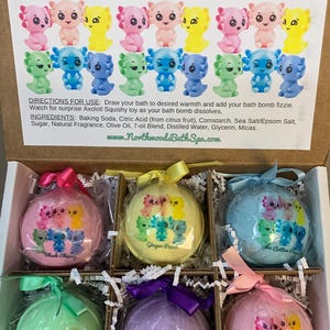 May include: A gift set of six bath bomb fizzies, each containing an axolotl squishy toy. The box includes bath bombs in various colors, each with a different axolotl design. The box also includes the text "Axolotl Squishies Bath Bomb Gift Set".