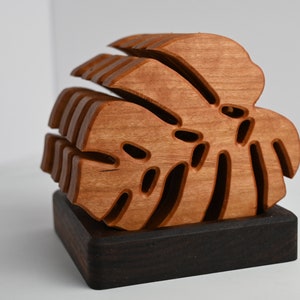 May include: A wooden sculpture of a monstera leaf, with intricate cutouts, is displayed on a dark wood base.