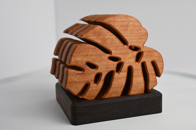 May include: A wooden sculpture of a monstera leaf, with intricate cutouts, is displayed on a dark wood base.