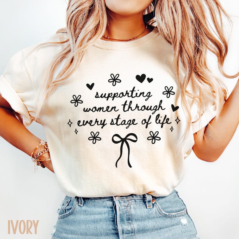 May include: A white t-shirt with the text "supporting women through every stage of life" in black lettering. The text is surrounded by small hearts, flowers, and a bow.