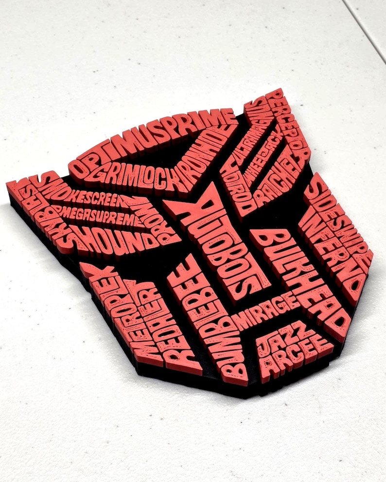 May include: A red and black emblem featuring the word "AUTOBOTS" and other character names. The emblem is a stylized shield shape, with the names of characters like Optimus Prime and Bumblebee.
