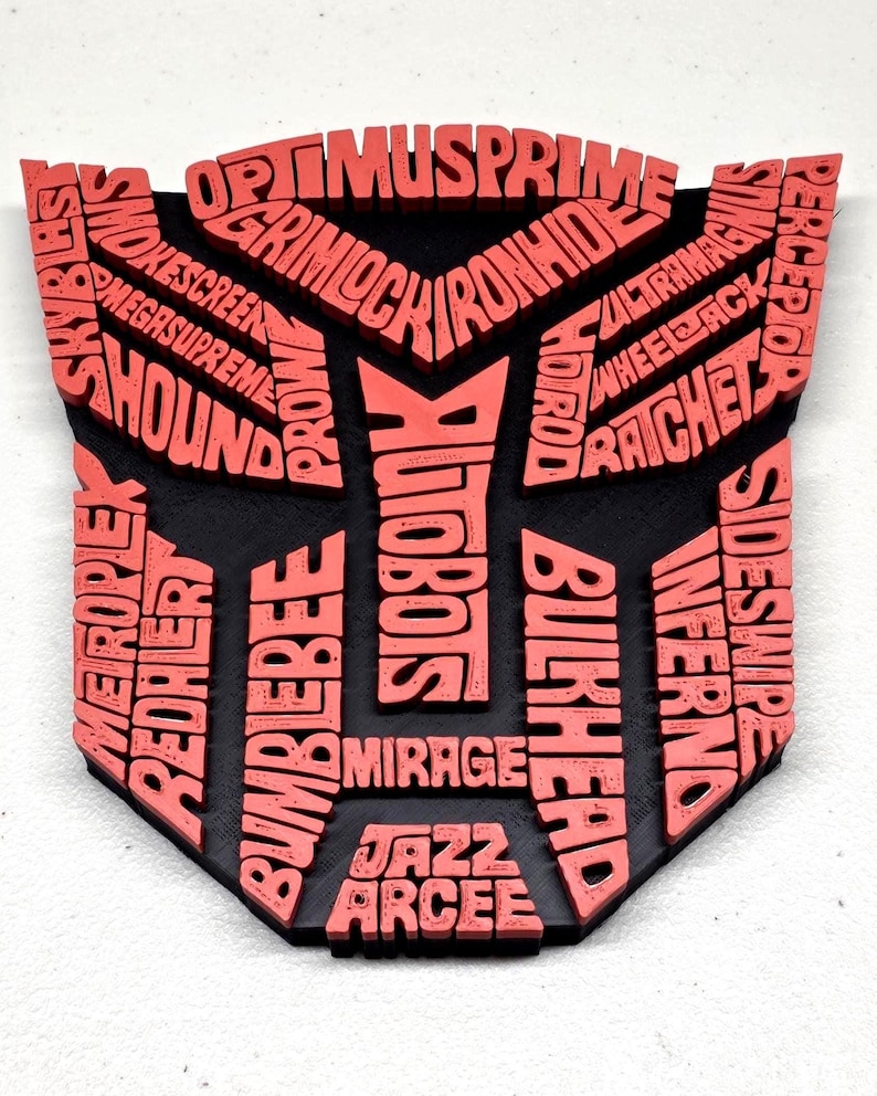May include: A black and red emblem featuring the names of Transformers characters. The red text includes names like Optimus Prime, Bumblebee, and Autobots, set against a black background. The design is a stylized shield shape.