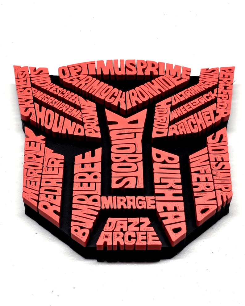 May include: A black and coral-colored Transformers logo featuring character names like Optimus Prime, Bumblebee, and Megasupreme. The logo is a shield shape with the names of the characters in a 3D effect.