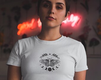 Puede incluir: Una camiseta blanca con un gráfico en blanco y negro de una polilla con un diseño de luna creciente.