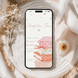 Puede incluir: Un smartphone muestra una invitación de cumpleaños con el texto "Chapter Two". La invitación presenta una pila de libros estilo acuarela con un lazo rosa. La invitación incluye el nombre, la fecha, la hora y la información de contacto de la cumpleañera.