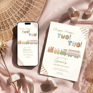 May include: A smartphone and a printed invitation with a train illustration and the text "Chugga chugga, TWO! TWO!" are displayed. The invitation is for Gian's 2nd birthday party. A decorative fan and ribbon are in the background.