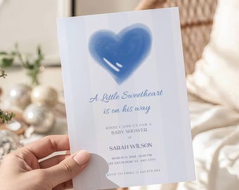 May include: A baby shower invitation held by a hand. The invitation features a blue watercolor heart and the text "A Little Sweetheart is on his way." Additional text includes the name Sarah Wilson, date, time, and RSVP information.