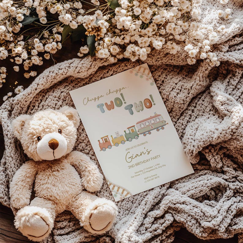 May include: A beige teddy bear sits next to a birthday party invitation. The invitation reads "Chugga chugga... TWO! TWO!" with a train illustration. The invitation is for Gian's 2nd birthday party.