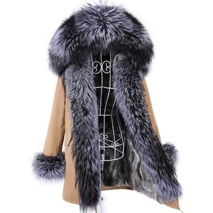 Może przedstawiać: Brązowy płaszcz typu parka z dużym, puszystym kapturem z futra srebrnego lisa i mankietami z futra. Futro jest grube i luksusowe, a płaszcz jest podszyty miękkim, ciepłym materiałem.