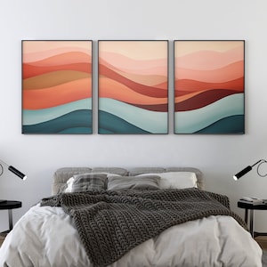 May include: Three abstract landscape paintings with a layered design of pink, red, orange, brown, blue and teal colours. The paintings are framed in black and hung above a bed with a grey headboard and a grey knitted throw blanket.
