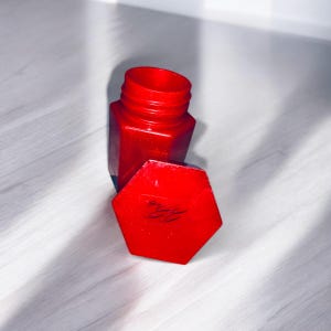 May include: A red hexagonal container with a red lid. The lid has a handwritten inscription on it.