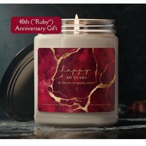 May include: A lit candle in a glass jar with a black lid. The label reads "happy 40 YEARS & cheers to many more" over a red and gold marble design. A banner at the top says "40th ("Ruby") Anniversary Gift".