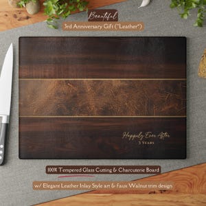 May include: A rectangular cutting board with a dark wood grain design and a leather inlay. The board has the text "Happily Ever After 3 YEARS" and "100% Tempered Glass Cutting & Charcuterie Board".