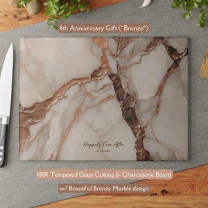 May include: A rectangular tempered glass cutting and charcuterie board featuring a white and bronze marble pattern. The board displays the text "Happily Ever After 8 YEARS" and is positioned next to a silver kitchen knife on a gray surface.