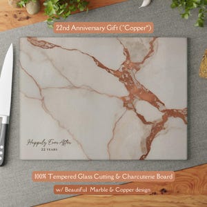 May include: A rectangular tempered glass cutting and charcuterie board featuring a white and copper marble pattern. The board includes the text "Happily Ever After" and "22 YEARS" printed in black on the lower left corner of the surface.