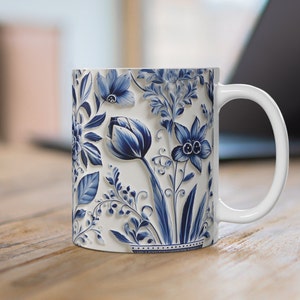 May include: White ceramic mug with a blue and white floral design. The design features tulips, leaves, and other flowers.