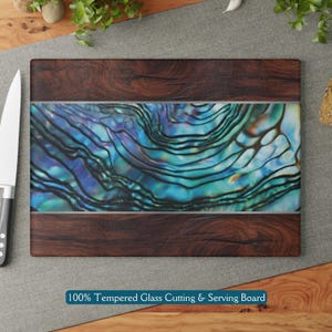 May include: A rectangular tempered glass cutting and serving board with a dark wood frame and a blue and green iridescent abalone shell design. The text "100% Tempered Glass Cutting & Serving Board" is printed below the board.