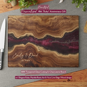 May include: A rectangular cutting board with a unique wood grain design, featuring a central band of deep red. The board is personalized with the names "Emily & David" and the text "40 Years". The text "100% Tempered Glass Cutting & Charcuterie Board" is also visible.