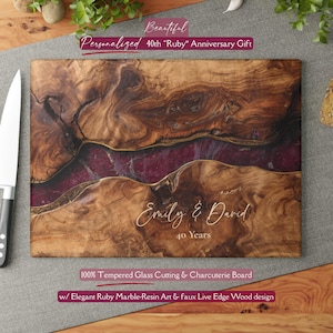May include: A rectangular tempered glass cutting and charcuterie board featuring a faux live edge wood design with a central deep ruby resin inlay. The board is engraved with the text Emily & David 40 Years in a white script and serif font.