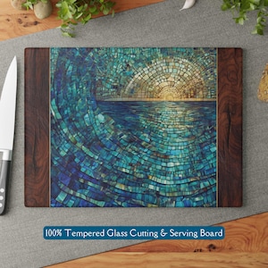 May include: A blue and gold mosaic glass cutting board with a wooden frame. The mosaic design depicts a wave crashing into the ocean with a sunset in the background. 100% Tempered Glass Cutting & Serving Board.