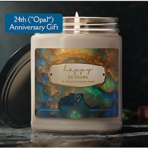 May include: A white soy wax candle with a gold and blue label. The label has the text "happy 24 YEARS & cheers to many more" and a heart symbol. The candle is in a clear glass jar with a lid.