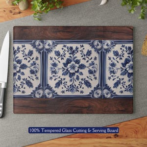 May include: A blue and white floral patterned tempered glass cutting board with a dark wood frame. 100% Tempered Glass Cutting & Serving Board.