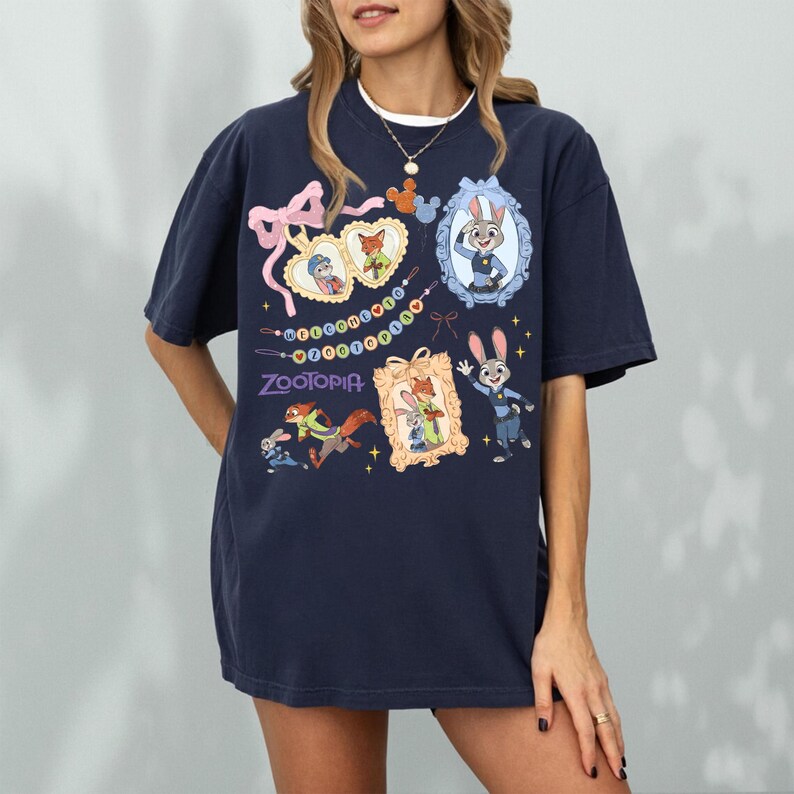 May include: Navy blue t-shirt with characters from the film Zootopia. The design includes framed images of Judy Hopps and Nick Wilde, and the word "Zootopia" in purple. The shirt has a relaxed fit.