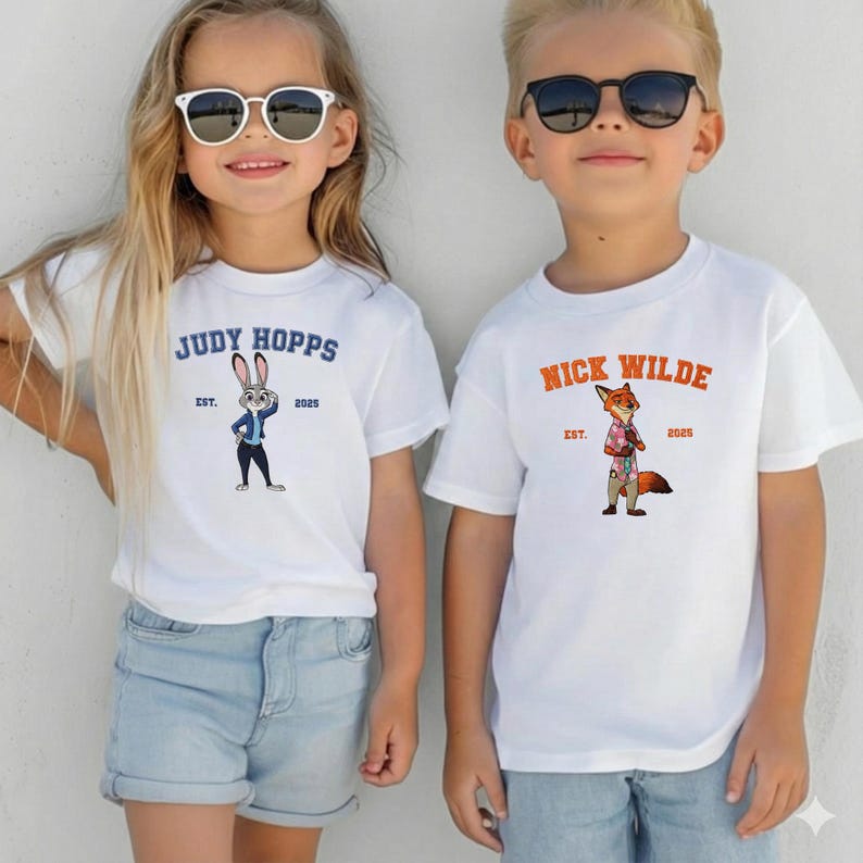 Puede incluir: Dos ni&ntilde;os con camisetas blancas con dise&ntilde;os de personajes de dibujos animados. Una camiseta dice "JUDY HOPPS" con una ilustraci&oacute;n de conejo, la otra dice "NICK WILDE" con una ilustraci&oacute;n de zorro. Ambas camisetas tienen "EST. 2025".