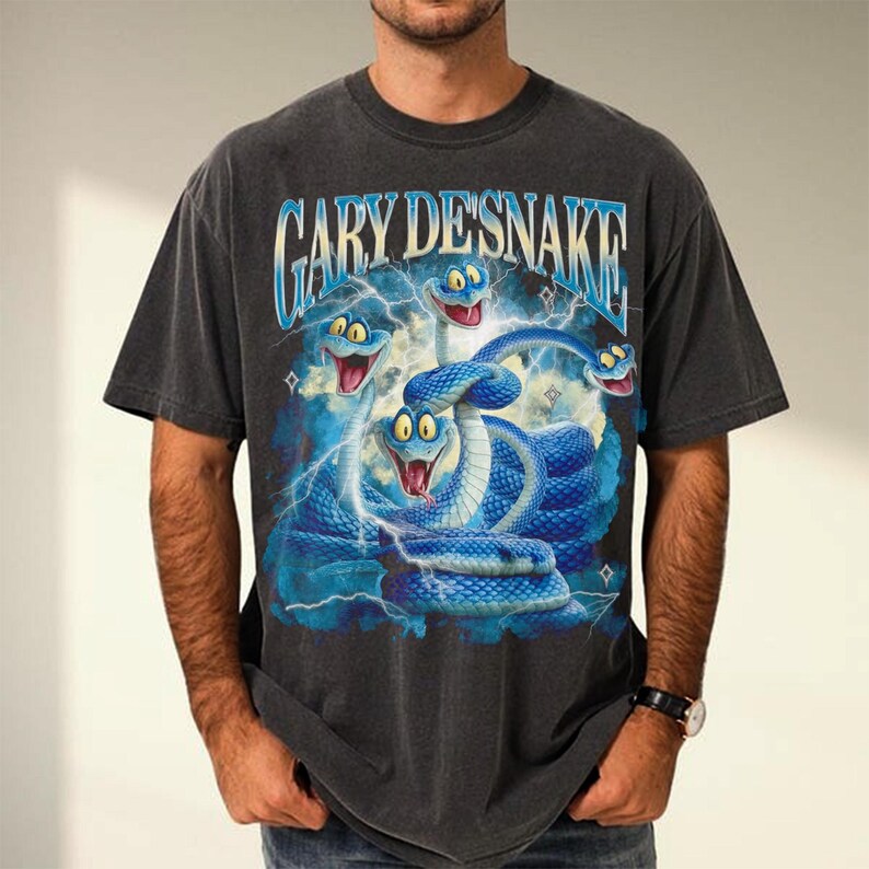 May include: Dark gray t-shirt featuring a blue and white graphic of snakes and lightning bolts. The text "GARY DESNAKE" is arched across the top. The shirt has short sleeves and a crew neck.