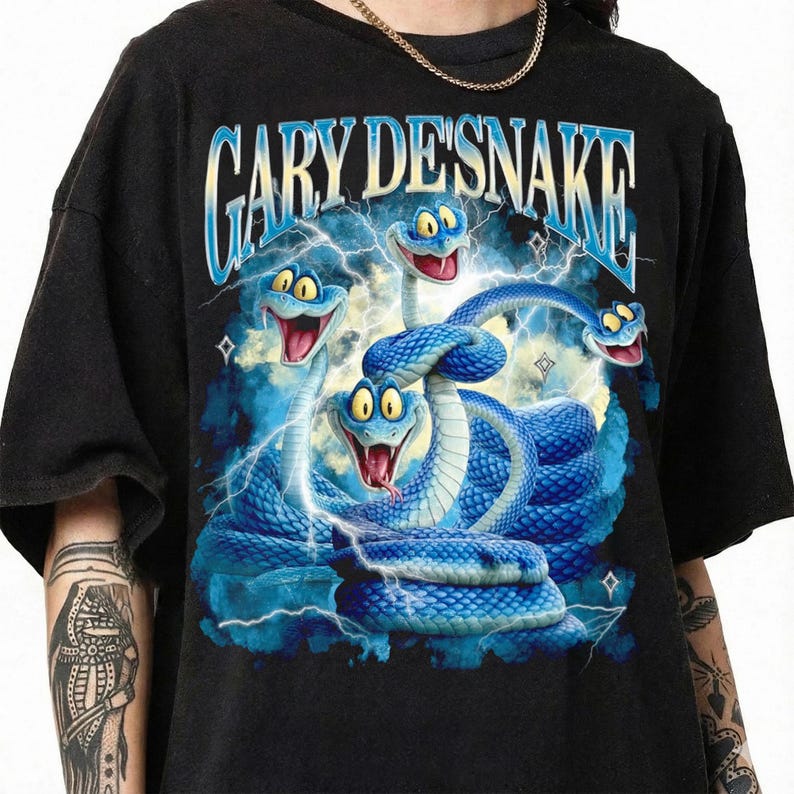 May include: Black t-shirt featuring a graphic of cartoon blue snakes with lightning bolts and the text "GARY DESNAKE" in a blue and white font. The snakes have yellow eyes and red tongues. The shirt has short sleeves.