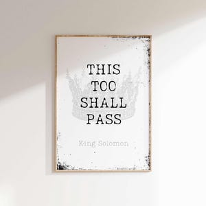 May include: A framed print with the words "THIS TOO SHALL PASS" in black, with a crown illustration above the text. The words "King Solomon" are below the text. The print has a distressed, vintage look.