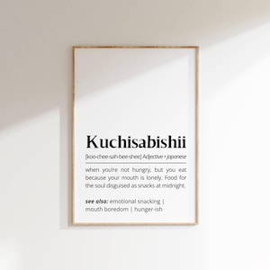 以下が含まれることがあります： 「Kuchisabishii」という日本語の単語とその定義が書かれた額縁入りのプリント。空腹ではないのに寂しさから食べることを説明しています。フレームは木製です。