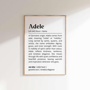 Könnte beinhalten: Ein gerahmter Druck mit dem Namen "Adele" und seiner Definition. Der Text beschreibt den germanischen Ursprung des Namens, seine Bedeutung und die damit verbundenen Eigenschaften wie Würde und Widerstandsfähigkeit. Der Rahmen ist hellbraun.