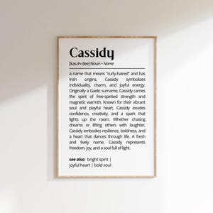 May include: A framed print featuring the name "Cassidy" and its definition. The text describes the name's meaning, Irish origins, and associated qualities like individuality and joyful energy.