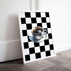 May include: A white framed print of a black and white chequered pattern with a white coffee cup filled with black coffee on a white saucer in the centre.
