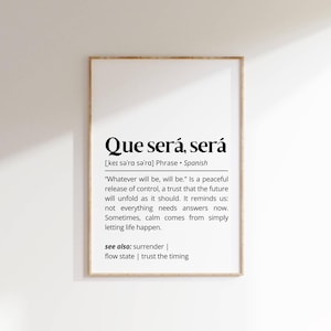 May include: A framed print with the phrase "Que será, será" in bold black font. The print includes a definition and related concepts like surrender and trust, all in black text on a white background.